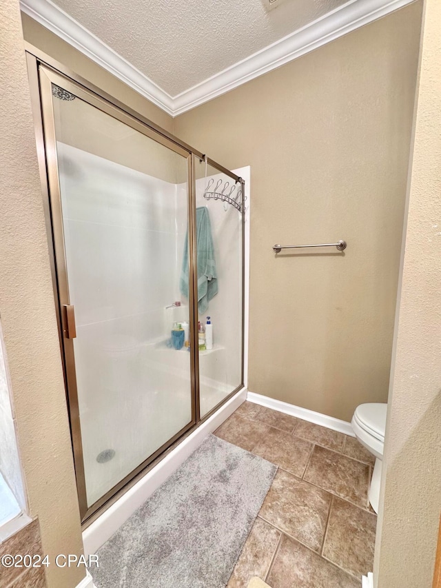 bathroom with a textured ceiling, toilet, a shower with door, and ornamental molding