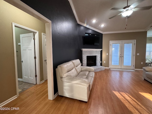 living room with french doors, light wood-type flooring, a brick fireplace, ceiling fan, and crown molding