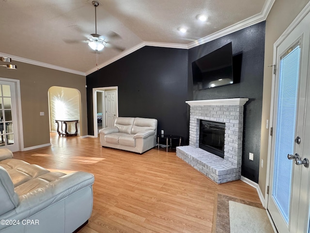 living room featuring lofted ceiling, a brick fireplace, light hardwood / wood-style flooring, ceiling fan, and ornamental molding