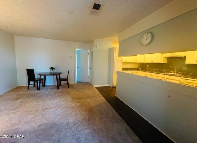 kitchen featuring sink, white cabinets, a textured ceiling, and dark colored carpet