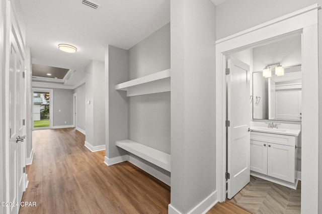 hallway with a tray ceiling, sink, and light wood-type flooring