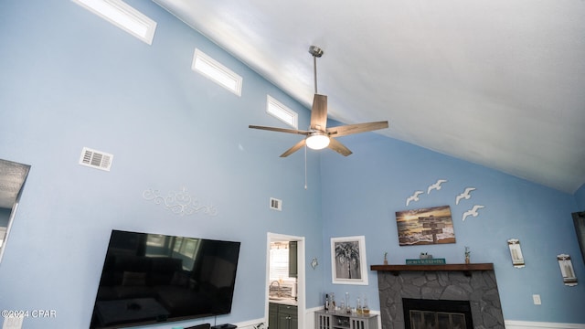 living room with ceiling fan, a stone fireplace, and high vaulted ceiling