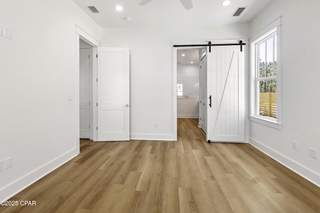 unfurnished bedroom with a barn door, visible vents, and light wood-style floors