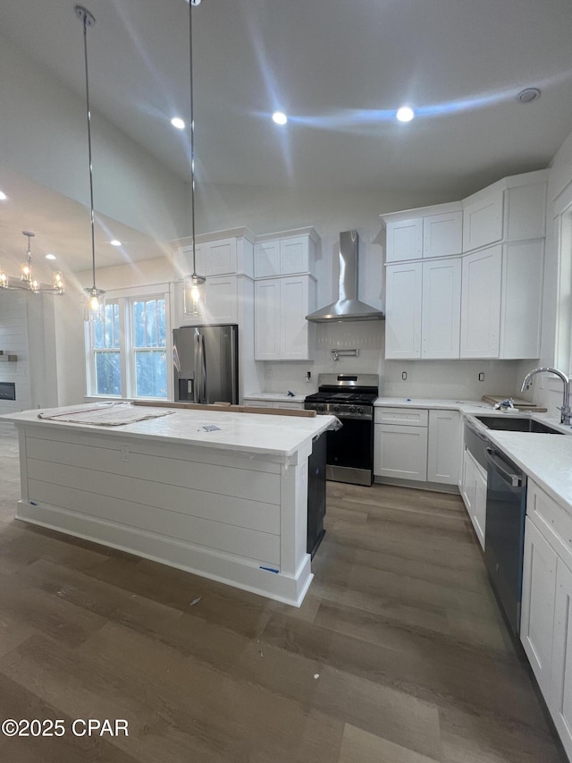 kitchen with a kitchen island, appliances with stainless steel finishes, white cabinetry, sink, and wall chimney range hood