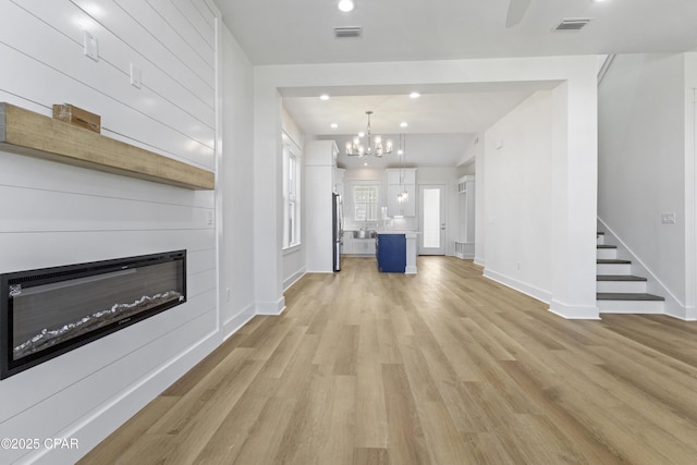 unfurnished living room with light wood finished floors, visible vents, stairs, a fireplace, and a notable chandelier