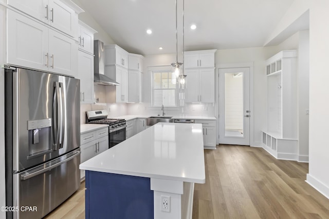 kitchen featuring stainless steel appliances, light countertops, light wood-type flooring, wall chimney range hood, and a sink