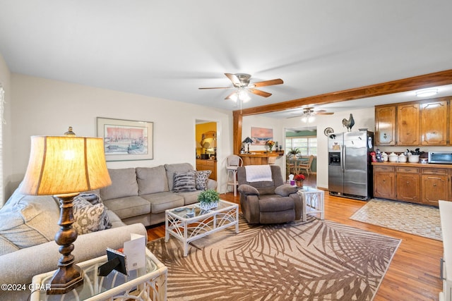 living room featuring ceiling fan, light hardwood / wood-style floors, and beam ceiling