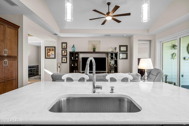 kitchen featuring light stone counters, decorative light fixtures, vaulted ceiling, and sink