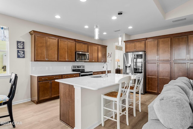 kitchen featuring sink, pendant lighting, a breakfast bar, a center island with sink, and appliances with stainless steel finishes