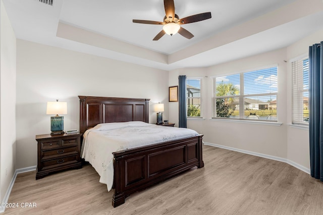 bedroom featuring ceiling fan, light hardwood / wood-style floors, and a tray ceiling