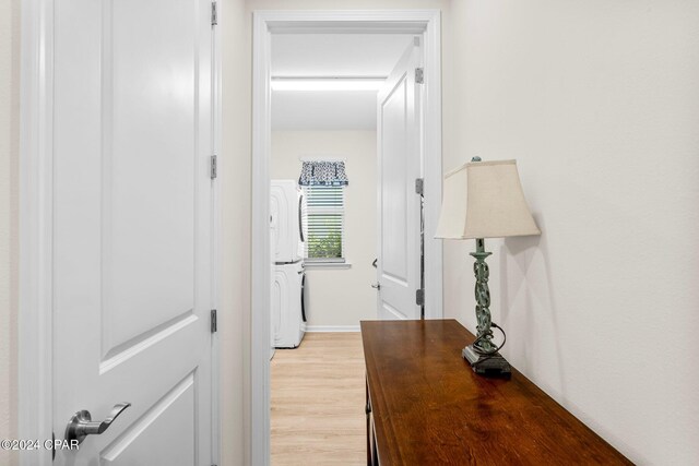 hallway with stacked washer and clothes dryer and light wood-type flooring