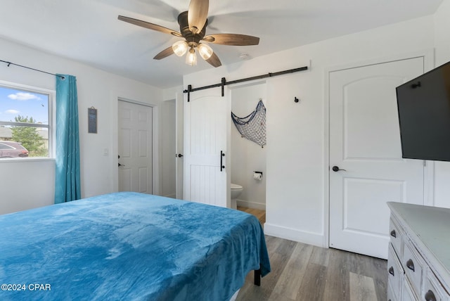 bedroom featuring light wood-type flooring, a barn door, ensuite bathroom, and ceiling fan