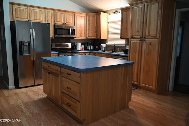 kitchen with appliances with stainless steel finishes, light hardwood / wood-style flooring, vaulted ceiling, and a kitchen island