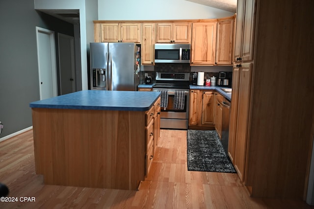 kitchen with light wood-type flooring, appliances with stainless steel finishes, vaulted ceiling, and a kitchen island