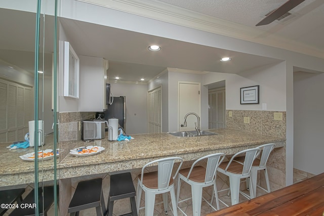 kitchen featuring sink, kitchen peninsula, crown molding, decorative backsplash, and white cabinets