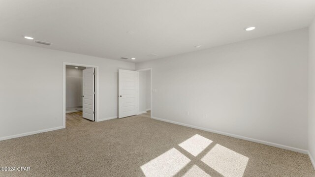 unfurnished bedroom featuring a walk in closet, light carpet, and a closet