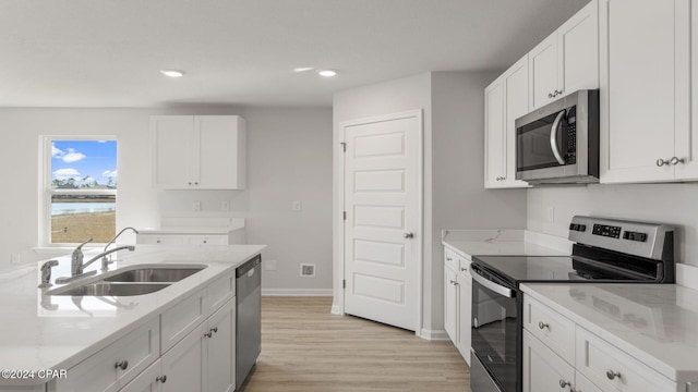 kitchen with a water view, sink, light stone countertops, appliances with stainless steel finishes, and white cabinetry