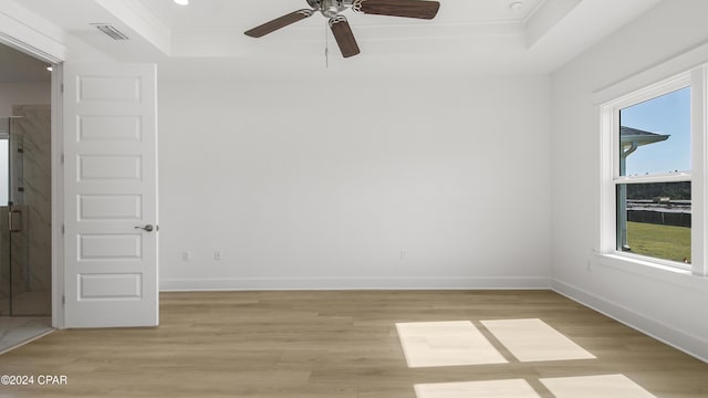 empty room featuring ceiling fan, light wood-type flooring, ornamental molding, and a tray ceiling