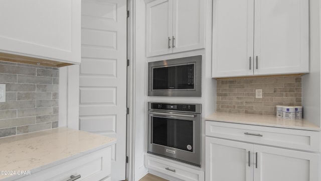 kitchen featuring backsplash, stainless steel appliances, white cabinetry, and light stone counters