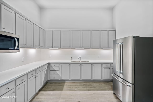 kitchen featuring sink, appliances with stainless steel finishes, gray cabinetry, a towering ceiling, and light hardwood / wood-style floors