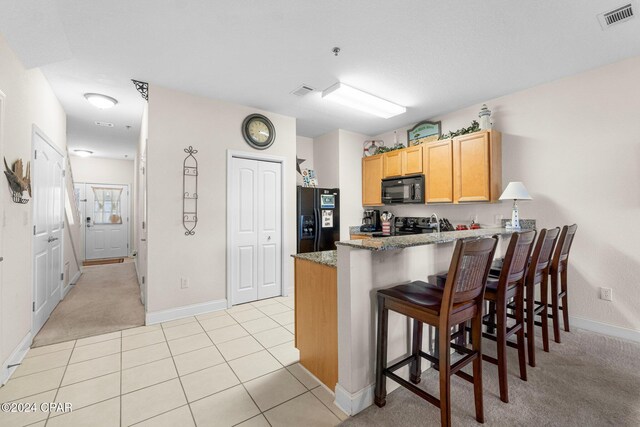 kitchen with visible vents, stone countertops, black appliances, a peninsula, and a kitchen breakfast bar