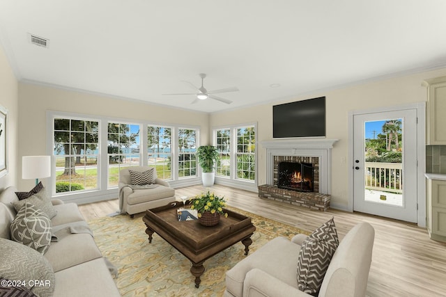 living room featuring light hardwood / wood-style floors, a brick fireplace, ceiling fan, and crown molding