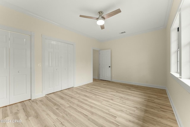 unfurnished bedroom featuring ceiling fan, light wood-type flooring, crown molding, and two closets