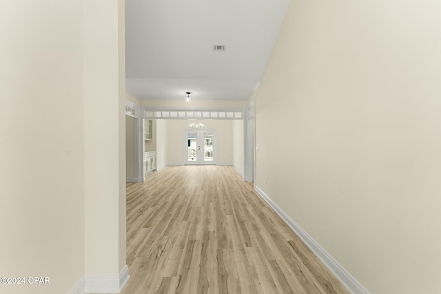 corridor featuring french doors, a chandelier, and light wood-type flooring