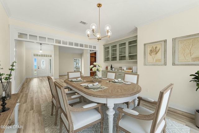 dining space with an inviting chandelier, ornamental molding, and light hardwood / wood-style flooring