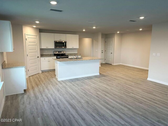 kitchen featuring stainless steel appliances, white cabinetry, plenty of natural light, and an island with sink