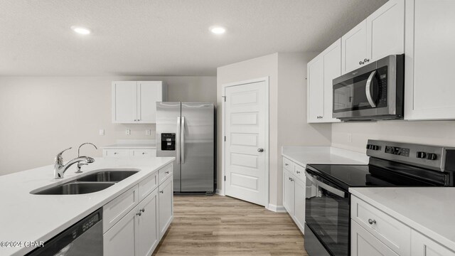 kitchen featuring appliances with stainless steel finishes, light wood-type flooring, a textured ceiling, white cabinets, and an island with sink