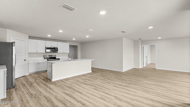 kitchen with white cabinets, appliances with stainless steel finishes, light wood-type flooring, and a center island with sink