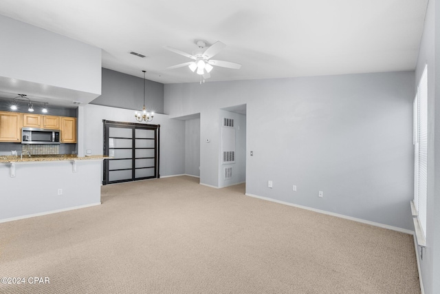 unfurnished living room featuring ceiling fan with notable chandelier, light carpet, and vaulted ceiling