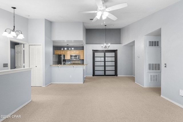 unfurnished living room featuring a towering ceiling, light colored carpet, and ceiling fan with notable chandelier