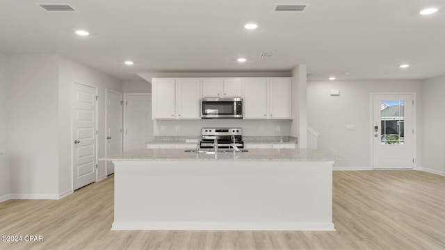 kitchen with light stone countertops, stainless steel appliances, a kitchen island with sink, light hardwood / wood-style flooring, and white cabinets