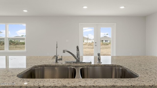 kitchen with plenty of natural light, light stone countertops, sink, and french doors