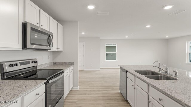 kitchen featuring light wood-type flooring, light stone counters, stainless steel appliances, sink, and white cabinetry