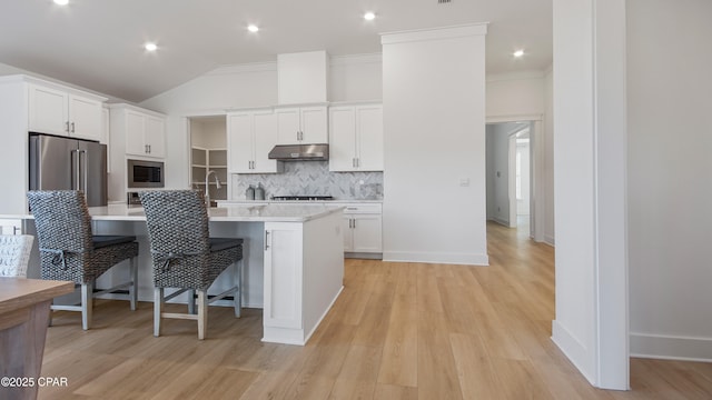 kitchen with appliances with stainless steel finishes, white cabinetry, lofted ceiling, a breakfast bar area, and a center island with sink