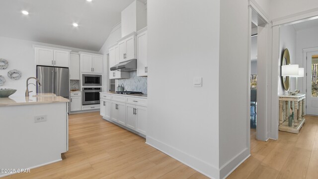 kitchen featuring appliances with stainless steel finishes, white cabinets, backsplash, a center island with sink, and light wood-type flooring