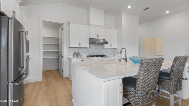 kitchen featuring tasteful backsplash, an island with sink, white cabinetry, stainless steel appliances, and light stone countertops