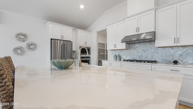 kitchen with lofted ceiling, white cabinetry, stainless steel appliances, light stone countertops, and decorative backsplash