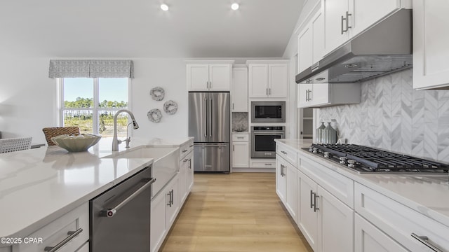 926 Crystal Bayou Blvd, Panama City Beach, FL 32407 - kitchen with under cabinet range hood, decorative backsplash, light wood-style flooring, appliances with stainless steel finishes, and white cabinetry