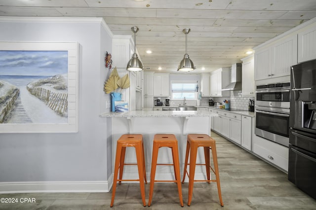 kitchen with white cabinetry, sink, wall chimney exhaust hood, a kitchen breakfast bar, and light stone counters