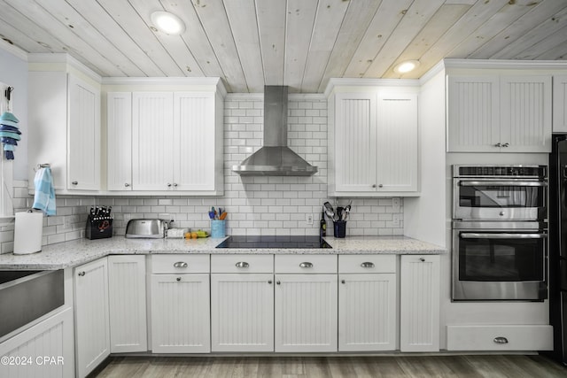 kitchen with black electric stovetop, wood ceiling, double oven, wall chimney range hood, and white cabinetry