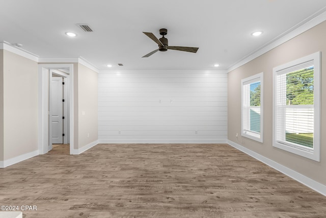 spare room featuring ornamental molding, light wood-type flooring, ceiling fan, and wooden walls