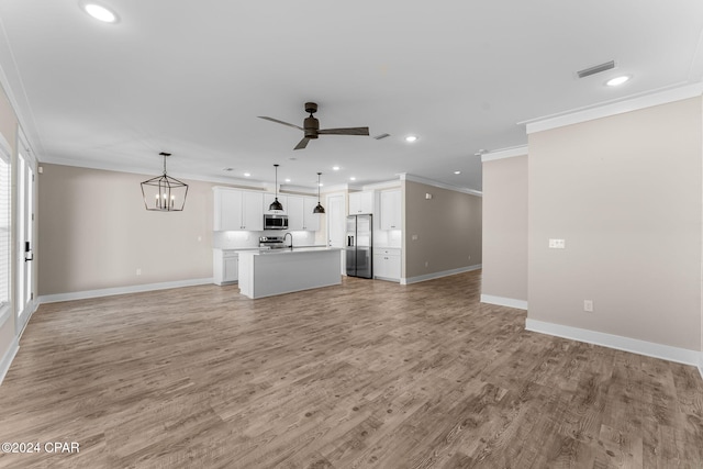 unfurnished living room featuring ceiling fan with notable chandelier, ornamental molding, sink, and light hardwood / wood-style flooring