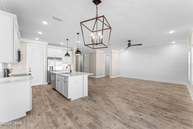 kitchen with appliances with stainless steel finishes, light wood-type flooring, white cabinets, hanging light fixtures, and an island with sink