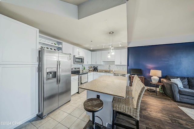 kitchen with a kitchen breakfast bar, appliances with stainless steel finishes, pendant lighting, white cabinets, and light wood-type flooring