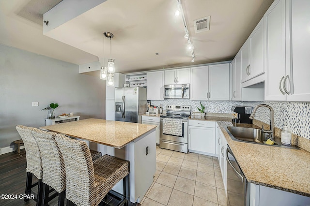 kitchen with stainless steel appliances, sink, pendant lighting, white cabinets, and a center island