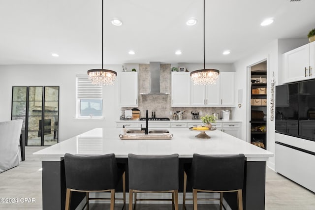 kitchen featuring a center island with sink, wall chimney exhaust hood, and pendant lighting